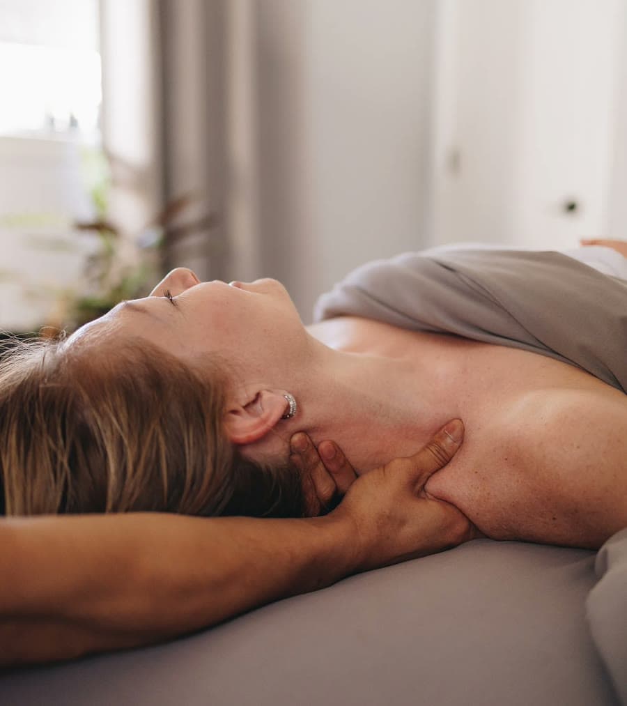 A therapist working along the neck and shoulder of someone lying face up on a table.