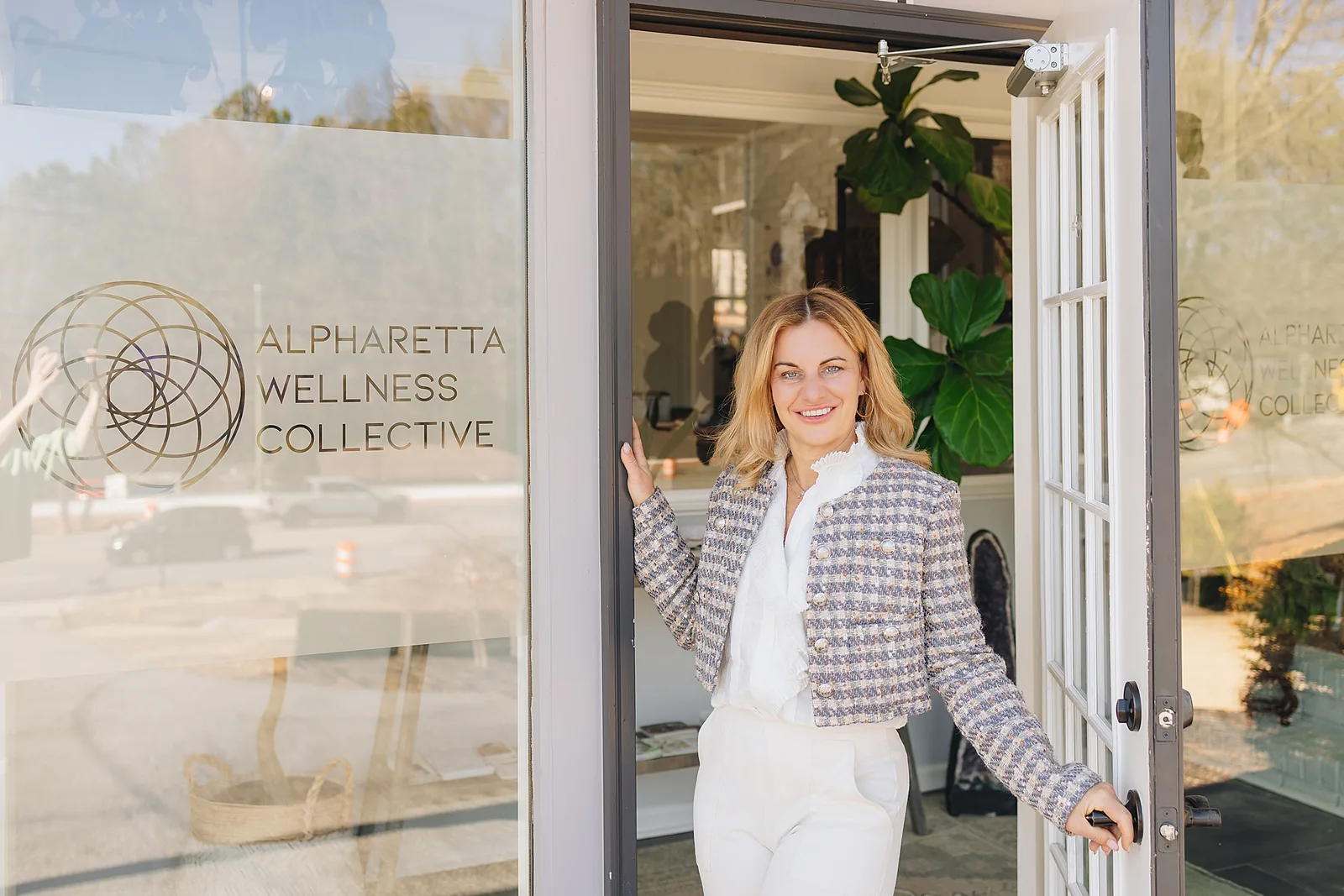 The front door of Alpharetta Wellness Collective held open, with the practice's mark etched into the glass.