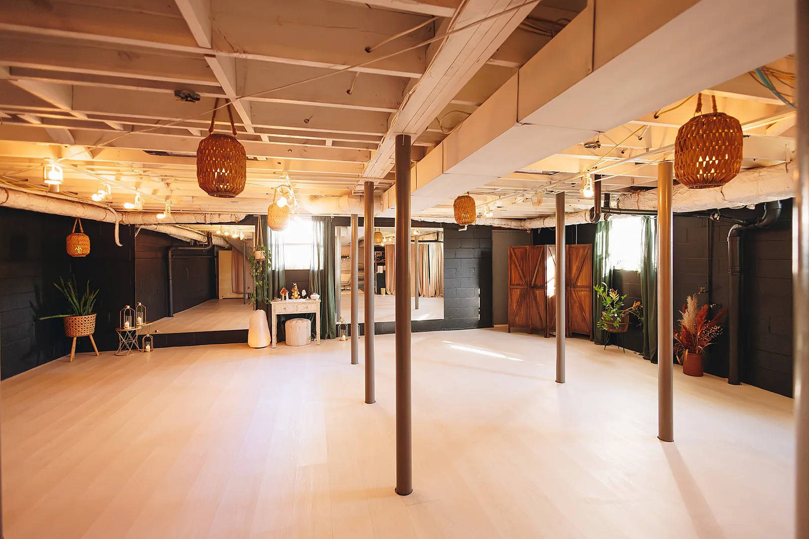 The Zen Den, wide: a long room with a pale wood floor, grey columns, wall mirrors and woven lanterns hung from the white-painted joists.